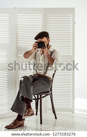 bearded man sitting on chair and taking pictures with vintage film camera 