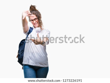 Young brunette student girl wearing backpack and headphones over isolated background smiling making frame with hands and fingers with happy face. Creativity and photography concept.