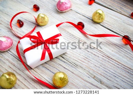 white gift box with red bow and hearts on white wooden background with gold bokeh, Valentines day gift.