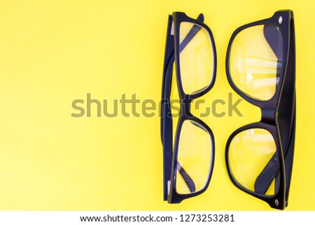 Two black eyeglasses on yellow uniform background view from above with the clear area of half photo for labels, headers. Concept photo of selection of glasses, optometrist work, shop of prescription