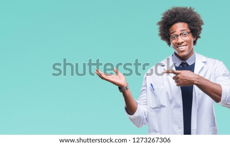 Afro american doctor scientist man over isolated background amazed and smiling to the camera while presenting with hand and pointing with finger.