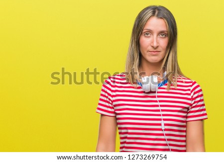 Young beautiful woman listening music wearing headphones over isolated background with serious expression on face. Simple and natural looking at the camera.