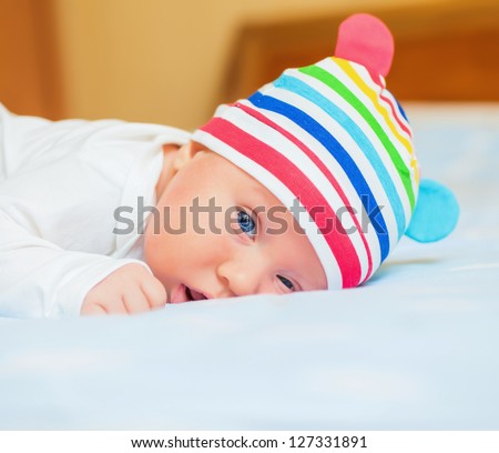 A cute little baby is looking into the camera and is wearing a white hat. The baby could be a boy or girl and has blue eyes. use it for a parenting or love concept.
