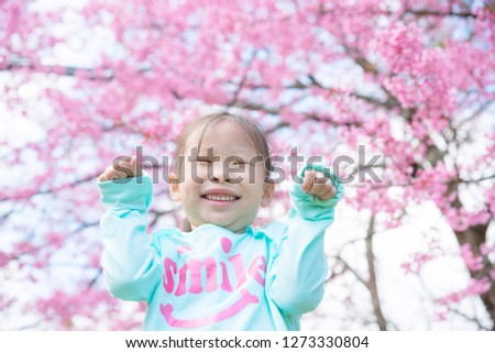 Little asian girl smiling in front of sakura tree. Little happy girl with blooming pink flower cherry tree.