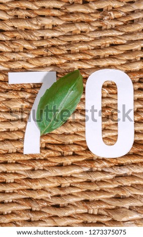 70 number seventy, graphic white digit and creative typography with leaf on rattan background