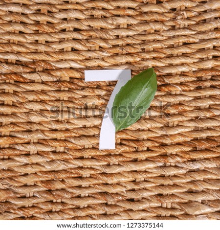 7 number seven, graphic white digit and creative typography with leaf on rattan background