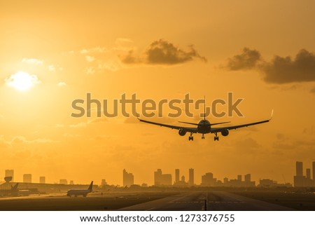 Airplane landing at Miami International Airport at sunrise with Miami Downtown skyline in the background.
