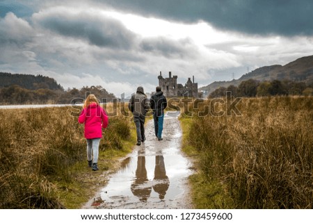 Three tourists walking towards castle at Autumn time on the Isle of Skye, Scotland, UK.