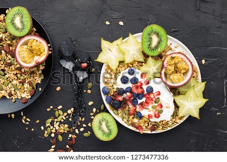 Super good breakfast snack. Yogurt with granola, kiwi, blueberries, passion fruit, carambola, pumpkin seeds, goji berries on a dark background. Top view