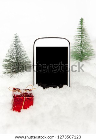 Mobile phone in the snow next to the gift and Christmas trees 