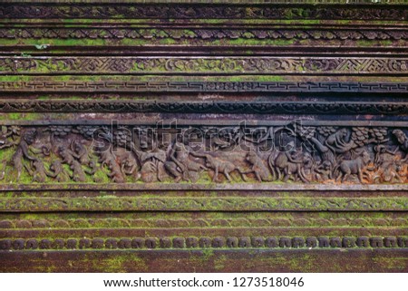 Mouldy tropical Balinese wall with traditional stone carved patterns covered with moss.