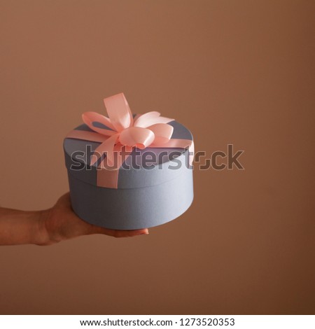 Beautiful round blue gift box with a pink bow in the hands of a woman
