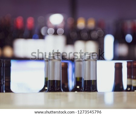 Close up of wine bottles in a row for sale, shop shelf with large group of bottles out of focus in background