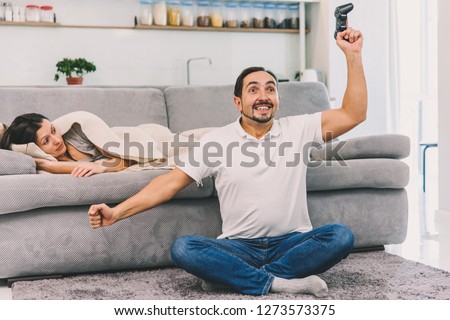 A man plays a game while his wife looks at him