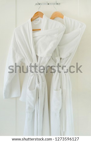 Two white coats hanging on the door. Hotel dressing gowns on the door hanger.