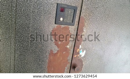 Texture, background, wallpaper of the intercom and its dial on the old brown or black metal wall, door or gate with lock and handle. The word "intercom" in Russian.