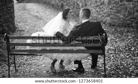 Young wedding romantic couple sitting on wooden bench in autumn deep forest outdoor on natural background, horizontal picture