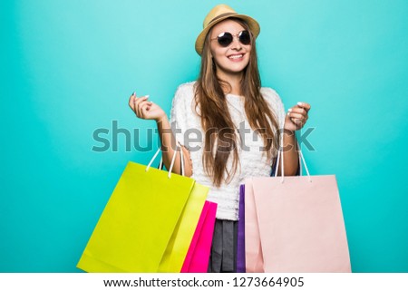 Photo of shopaholic woman in straw hat holding colorful paper shopping bags with purchases isolated over blue background