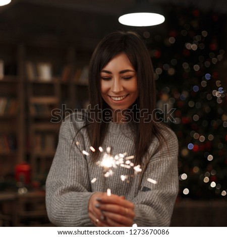 Young happy woman in a knitted sweater holds an amazing sparkler in her hand in a vintage room. Merry Christmas and Happy New Year. Girl smiling.