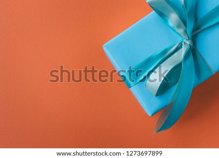 Top view of a gift wrapped in blue paper with a blue satin ribbon on orange background with copy space. Birthday, Mother's or Valentine's day present concept