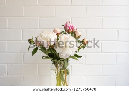 Close up of white peonies in glass vase against painted brick wall (selective focus)