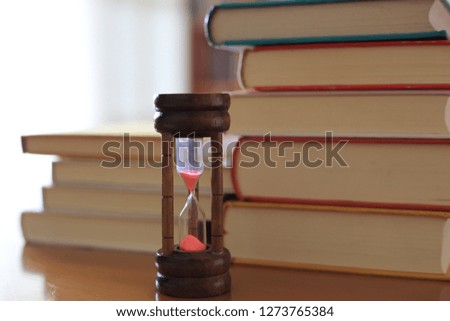 Close-up of hourglass on table in library book stack is the background selective focus and shallow depth of field
