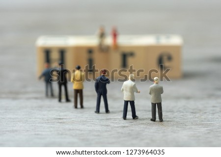 Miniature people, candidates and wooden word block "HIRE". Human resource concept, recruiting, hiring process.