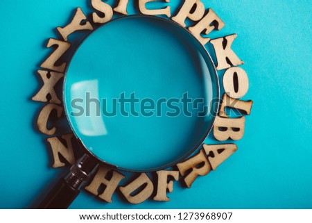 Magnifying with wooden alphabets around on the blue background.