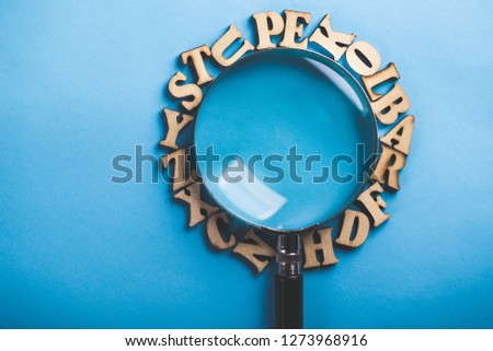 Magnifying with wooden alphabets around on the blue background.