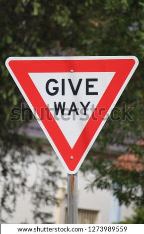 "Give way" street signage indicating to drivers to give way ahead with trees in the background