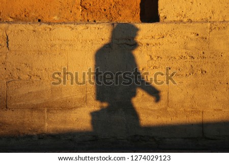 Front view of the silhouette of a lonely man walking in a street. Figure of a male pedestrian projected on a brown stone wall. Shadow of a person drawn on a rough textured surface in a french city.
