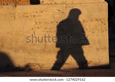 Front view of the silhouette of a lonely man walking in a street. Figure of a male pedestrian projected on a brown stone wall. Shadow of a person drawn on a rough textured surface in a french city.