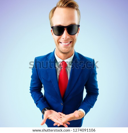 So what?! Funny young businessman in sunglasses, confident suit and red tie, on blue background. Business concept.