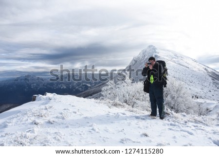 Hiker with backpack and camera taking picture of snowy mountain. Winter mountain landscape, Happy tourist hiking in winter 