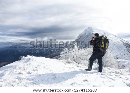 Hiker with backpack and camera taking picture of snowy mountain. Winter mountain landscape, Happy tourist hiking in winter 