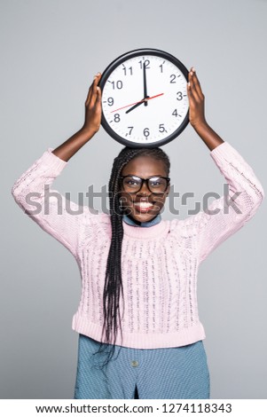 Portrait of happy afro american woman standing with clock on gray background