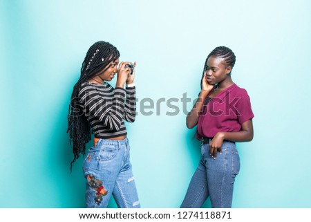 Picture of one african girls taking photos on camera of other african girl isolated over green background