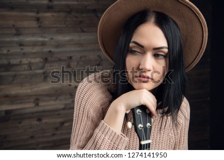 Close up portrait of young caucasian woman playing ukulele in front of a wooden background. Studio shot, leisure activities concept.