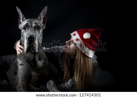 dog the Great Dane with the girl in a cap of Santa Claus on a black background