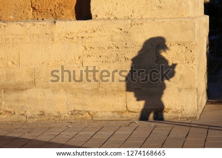 Close up front view of the figure of a lonely woman walking in a french street. Sihouette of a female person drawn on an ancient stone wall. Shadow of a pedestrian projected on a textured surface.