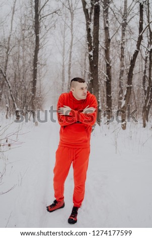 Crazy guy posing in the forest in the winter, on the background of snow and trees. A man in a red tracksuit walking in the fresh air. Concept: walking and training outdoors in the cold
