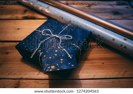 Close up of a gift wrapped present in blue and gold star design paper with white and gold string / bow and a gift tag. On a wooden table ready for the holidays. 