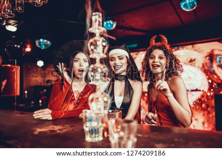 Women in Costumes Looking at Flaming Cocktail. Group of Smiling Young Friends Wearing Costumes Excited about Flaming Cocktails on Bar counter in Nightclub. Celebration of Halloween