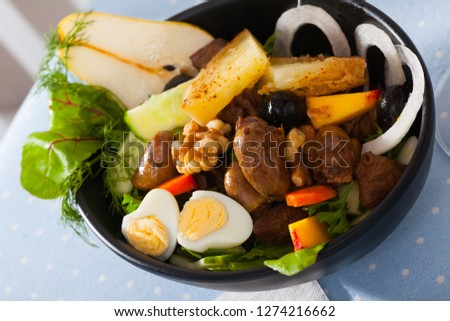 Closeup of salad of chicken hearts with peach, pear, fried cheese and quail eggs served in black bowl