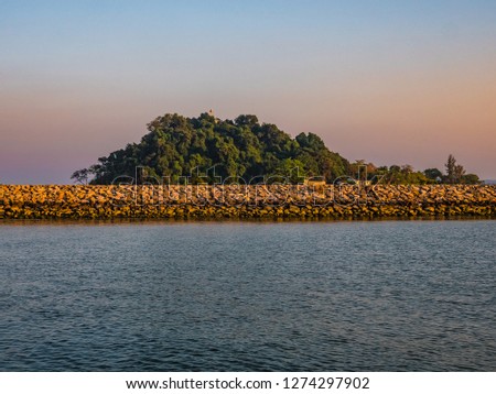 Beautiful picture of a stone wall in the sea and a huge wooded area behind it in Thailand.