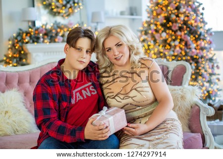Beautiful mother and her son are sitting together on sofa in cozy room with Christmas tree and fireplace