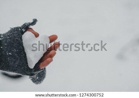 A man is holding snow in the shape of the heart in his hand in grey glove. White snow on the background. Focus is on the heart. Winter season in the park. Symbol of love in the hands.