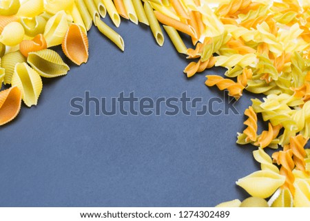 Frame of raw three-color pasta: tomatoes, spinach and wheat paste. Place for text (recipe). Food background.  