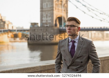 Portrait of the elegant young man who is standing outdoor against the background of river and bridge