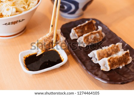 Gyoza (Japanese Pan-Fried Dumplings) held by chopsticks served with sauce and sesame oil.